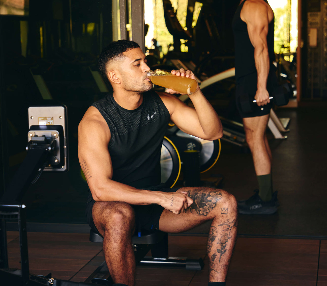 Photo of athletic man sitting on a bench drinking Moxie at a gym