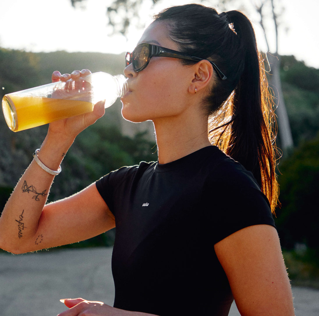 Photo of athletic woman drinking Moxie out of a glass bottle outdoors