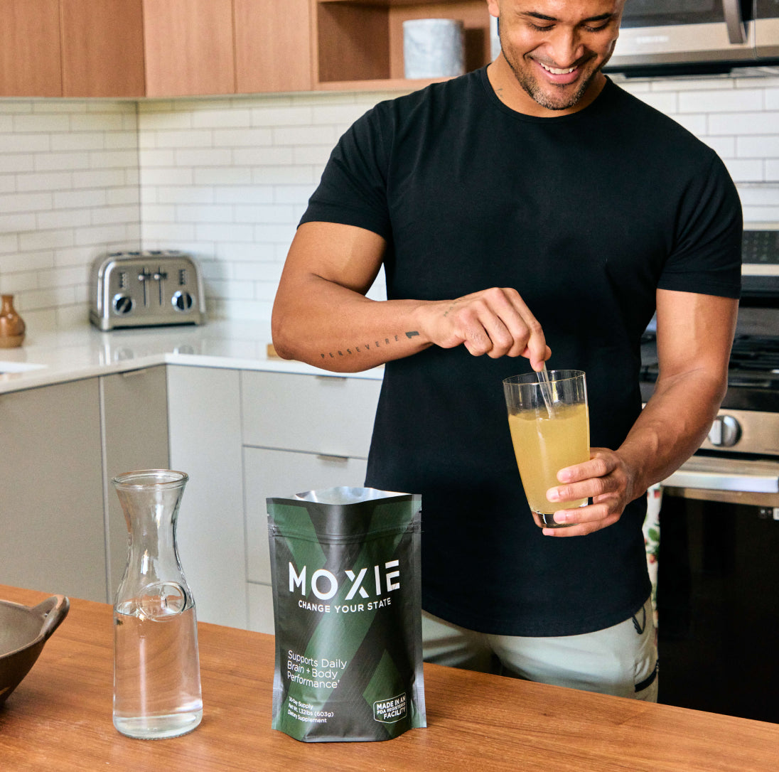 Photo of athletic man in a kitchen stirring Moxie in a glass of water