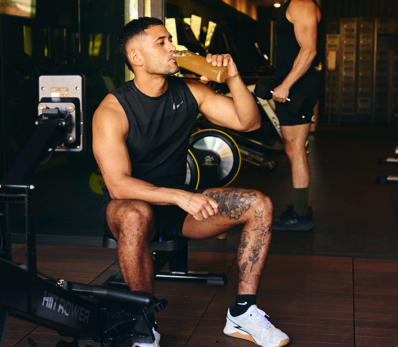 Photo of man sitting down drinking Moxie supplement out of a glass bottle at the gym